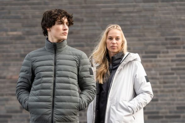 A woman and a man in casual winter jackets in front of a wall