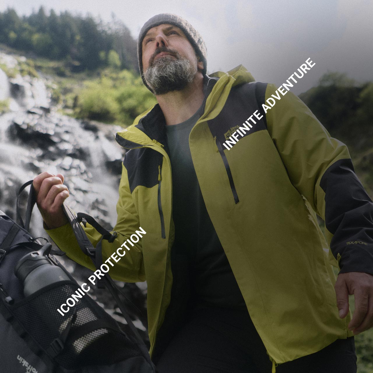 A man in a yellow jacket and beige beanie stands outdoors with a backpack, looking up. Text reads "Iconic Protection" and "Infinite Adventure"